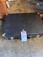 Closed black hard case with metal corner protectors and latches, auction label taped to front