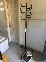 Full view of black metal coat rack with multiple hooks and part of bathroom scale at base