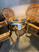 Photo showing round glass-top rattan table with 4 rattan chairs with black cushions surrounding it.