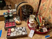 Initial overview photo showing mixed candles in different colors and shapes, brass candle holders, white ceramic holders, and round wall clock on table