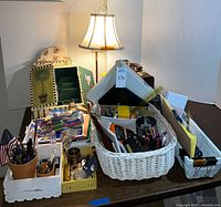 Wide view of assorted office and desk accessories including baskets, trays, pens, and a lamp in the background.