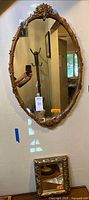 Large oval mirror showing full ornate gold-tone wood frame with floral carvings and reflective glass surface, hung on wall
