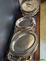 Various stacked ornate silver-plated platters and trays of different sizes and styles showing tops and edges