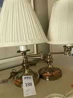 Pair of brass reading lamps with articulating arms and pleated white or cream shades.