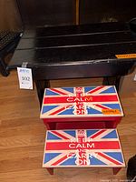 Two wooden step stools shown; smaller 'Keep Calm and Carry On' themed stool in front of a larger plain black wooden stool.