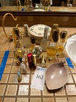 Perfume bottles, lipstick tubes, and soapstone leaf-shaped soap dish arranged on countertop