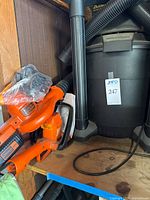 Black & Decker electric blower and hedge trimmer sitting next to black Shop-Vac main unit on wooden shelf