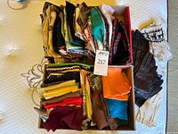 Two cardboard boxes filled with folded scarves and gloves arranged at front on mattress.