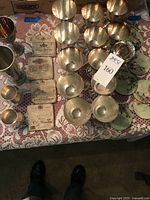 Overview photo showing multiple silver plated goblets, tumblers, and rectangular vintage wine label stone coasters arranged on a lace tablecloth.