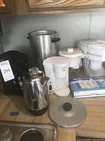 Overview of lot including black Black & Decker coffee maker, two Brita pitchers, Farberware electric kettle, vintage percolator, and box of Brita filters.