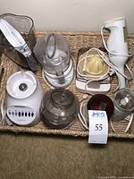 Lot of small kitchen appliances including Oster food processor, coffee grinders, hand blender, and citrus juicer in a wicker basket.
