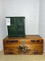 Wide view showing the tiny green chest of drawers on top of the natural wood field box with duck etching and printed text