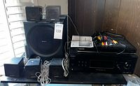 Sony subwoofer with 5 small Sony speakers and Sony receiver, Samsung DVD player, cables and remotes all boarded on a table.