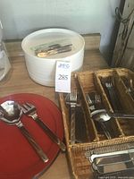 Photo showing white plastic plates stacked with flatware utensils on top alongside red plastic plates with black edges and stainless steel serving utensils.