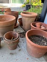 Various terracotta and clay pots stacked and arranged outdoors, some containing soil or dried leaves.