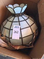 Light fixture in cardboard box, showing the globe shade with stained and opaque glass and metal leading, with rounded petal design at the top