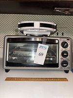 Front view of Black+Decker toaster oven with sandwich maker placed on top, showing control knobs and glass door.
