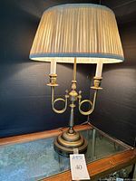 Full side view of traditional brass candelabra lamp with two bulb holders and pleated cream-colored shade.