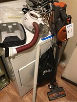 Lot showing three vacuum cleaners including Sunbeam handheld, Shark upright, with hose and power cord visible, and various accessories.