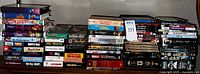 Photo of stacked VHS, DVD, and Blu-Ray movies showing a variety of genres and titles in original cases, with visible wear suggesting used condition.