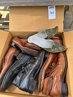 Box containing four pairs of men's leather shoes in brown and black, including boots and dress shoes, shown piled in a cardboard box.