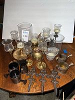 Photo showing an assortment of metal and glass home decor including candle holders, mini watering cans, wall hooks, and vases arranged on a wooden table.