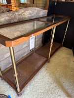 Full side view of console table showing wooden frame, brass legs, glass top, and cane lower shelf.