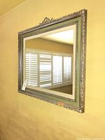 Full view of the ornate vintage wood wall mirror hanging on a yellow wall, showing carved details and distressed finish.