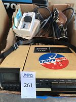 Photo of the Akai VT-100 video tape recorder with shoulder strap, cables, and other accessories packed in a box