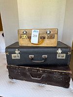Three vintage suitcases stacked together showing black, brown, and ivory colors and handle and latch details.