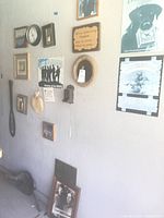 Photo showing a cluster of diverse vintage styled wall decor items including framed photos, plaques, a clock, and unique items like a wooden oar and black decorative objects.