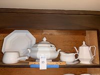 White serveware set on wooden shelf showing octagonal teapot, soup tureen with lid, platter, melting pot and gravy bowl