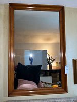 Full view of rectangular wall mirror with medium brown wooden frame hung on wall, reflecting room contents