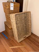 Set of four baskets showing three lidded wicker/rattan baskets stacked upstairs with a large open sisal basket leaning vertically in foreground.