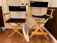 Two wooden folding director's chairs with black canvas seats and backs, one taller than the other, with two off-white replacement canvases placed in front.