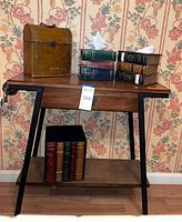 Full view of wooden table with drawer, leather-look chest, two sets of faux book tissue holders, and decorative box on top, with floral wallpaper background.