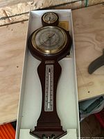 Instrument in box showing full view of wood plaque with thermometer and dials