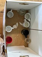 Top-down view of box showing eight assorted ceramic and glass mugs