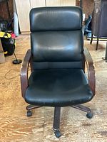 front view of black faux leather office chair showing seat, backrest, wood armrests and base