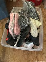 Plastic bin containing assorted shoes in plastic wrapping