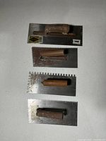 Four notched trowels laid out showing notch patterns, handles, overall wear