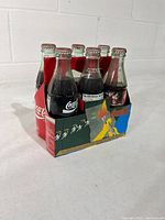 Front view of six unopened Coca-Cola bottles in cardboard carrier