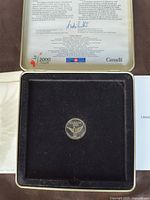 Commemorative metal tin containing a Canada United Nations peace coin in black velvet display with certificate and official inscriptions inside the lid.