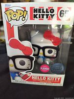 Front view of boxed Hello Kitty Funko Pop! figure showing the character with black glasses and red bow, box labeled with number 65 and flocked sticker.