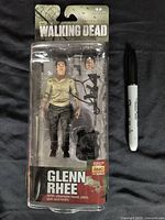 Glenn Rhee The Walking Dead action figure sealed on original card with accessories and packaging shown alongside marker for scale.