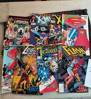Photo shows a lot of 8 vintage comic books including Legion of Super-Heroes Illustrated Index, two X-Men comics, Superman Man of Steel, Flash, Legion, Arak, and a Colossus comic. Comics have colorful covers and are in mostly high grade condition.