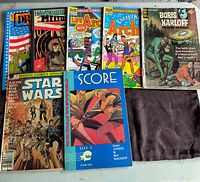 Shows 7 comic books with varied titles and covers, plus a black cloth/bag item