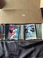 Open box showing a large collection of sports cards separated into two sections: mostly football cards on the left and baseball cards on the right. Cards are upright and tightly packed in a cardboard box.