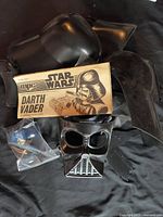 Black molded plastic parts for Darth Vader helmet, both large and small pieces, laid out on black fabric background with original MPC brand printed instruction sheet.