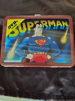 Photo showing the front of the metal lunch box with colorful Superman graphic and text indicating DVDs inside.